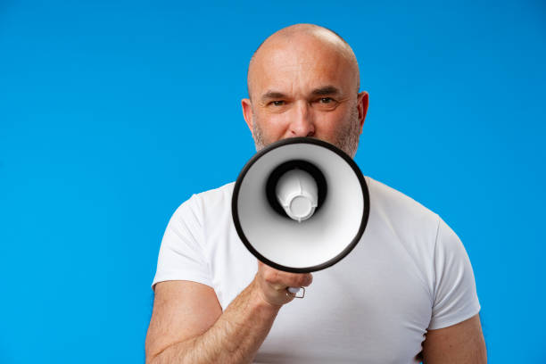 istock Middle-aged man speakng into megaphone against blue background 1405915558