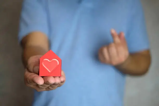 Photo of Man hand holding red house with heart and blur of hands making small heart.