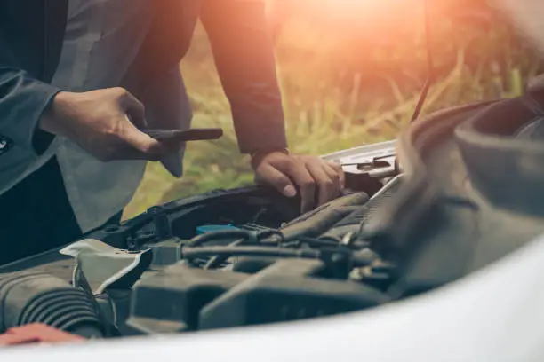 Photo of Business man using mobile phone while looking at broken down car on road.