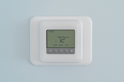 Photograph of a modern residential programmable heating and cooling thermostat set at 72 degrees mounted on a blue wall