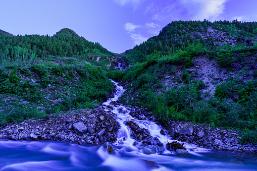 Mountain Stream Flowing Into River - Scenic landscape with dramatic high peaks with water flowing softly into another flowing body of water in wilderness area in the Rocky Mountains.