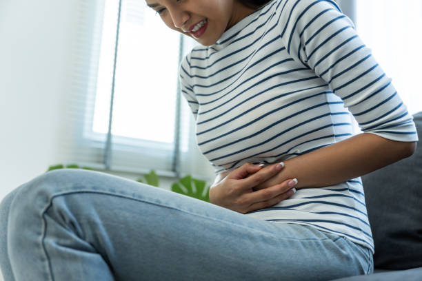 Asian beautiful sick girl suffer from hurt stomachache in living room. Attractive young woman feel bad and painful after wake up on bed, having stomach ache or periods then clasping belly in morning. hermosa chica enferma asiática sufre de dolor de estómago herido en la sala de estar. la mujer joven atractiva se siente mal y dolorosa después de despertarse en la cama, tener dolor de estómago o períodos y luego apretar el vientre por la mañana.