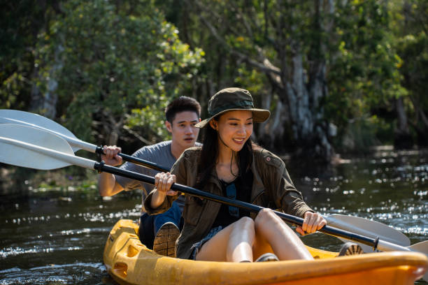 Asian attractive romantic young couple rowing kayak in a forest lake. Backpacker man and woman travel and kayaking on canoe in beautiful mangrove forest enjoy spend time on holiday vacation together. Asian attractive romantic young couple rowing kayak in a forest lake. Backpacker man and woman travel and kayaking on canoe in beautiful mangrove forest enjoy spend time on holiday vacation together. couple punting stock pictures, royalty-free photos & images