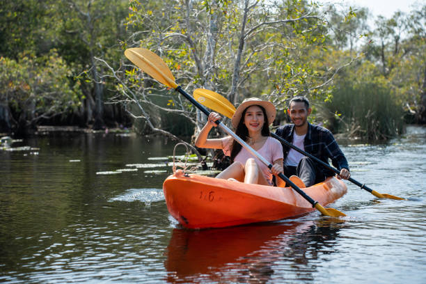 Asian attractive romantic young couple rowing kayak in a forest lake. Backpacker man and woman travel and kayaking on canoe in beautiful mangrove forest enjoy spend time on holiday vacation together. Asian attractive romantic young couple rowing kayak in a forest lake. Backpacker man and woman travel and kayaking on canoe in beautiful mangrove forest enjoy spend time on holiday vacation together. couple punting stock pictures, royalty-free photos & images