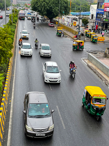 Noida Expressway, India - June 22, 2022: Stock photo showing traffic including cars, auto rickshaws, buses, vans and motorcycles driving on Noida expressway with yellow and black hazard stripes on central reservation concrete wall, as viewed from road bridge.
