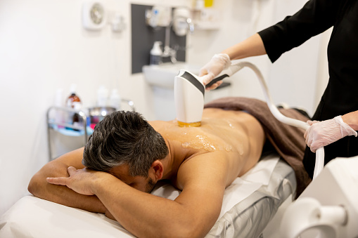 Handsome man getting a hair removal treatment on his back at a spa - beauty treatment concepts