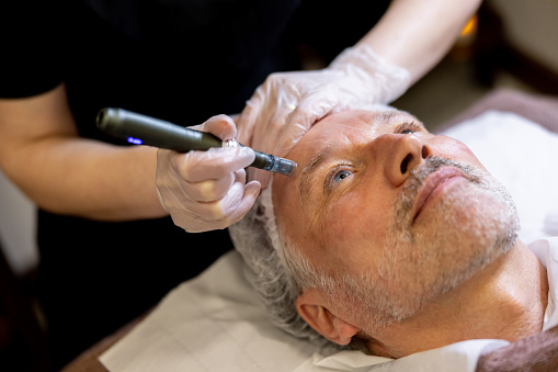 Handsome senior man at the spa getting an anti aging treatment on his face - beauty concepts