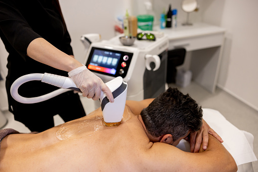 Handsome man getting a laser hair removal on his back at a spa - beauty treatment concepts