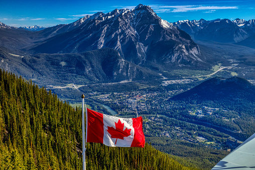 A Canadian flag with a panoramic view of Banff and rocky mountains during the morning