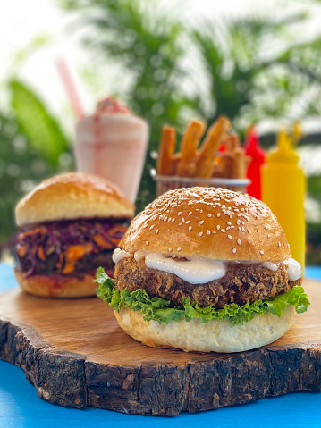 Stock photo showing outdoor, gastro pub restaurant scene. Turquoise table top with homemade beef burgers served in sesame seed bread buns with melted cheddar cheese, tomato ketchup, red cabbage coleslaw and lettuce on a wooden platter.