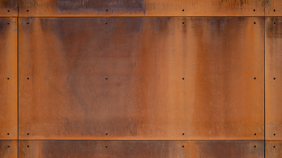 Grunge brown orange rusty corten steel facade wall with rivets, rust metal texture background