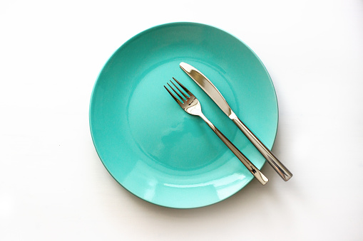 Empty green plate and stainless knife and fork isolated on white background. Served cutlery. Top view