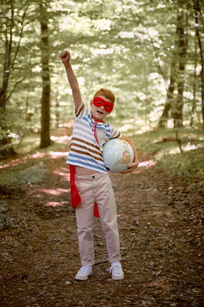 istock Ginger caucasian boy wearing superhero costume with globe in the forest 1405945995
