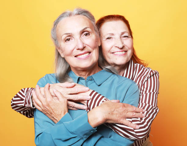 istock Two pretty older women hugging on yellow background 1405947798