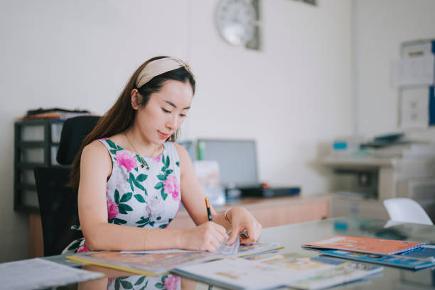 studente di insegnamento scolastico femminile cinese asiatico che segna i lavori sulla sua scrivania sul suo posto di lavoro - grading teacher desk writing foto e immagini stock