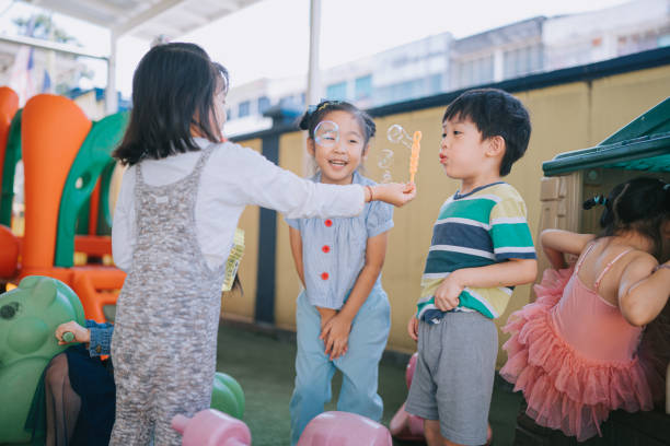 azjatycki chiński przedszkolak bańkę na placu zabaw bawiący się z kolegą z klasy po szkole - bubble wand child blowing asian ethnicity zdjęcia i obrazy z banku zdjęć