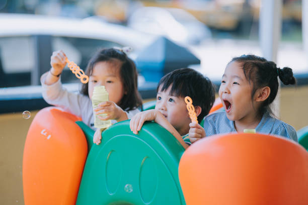 放課後にクラスメートと遊ぶ遊び場で泡を吹くアジアの中国の就学前の生徒 - bubble wand child blowing asian ethnicity ストックフォトと画像