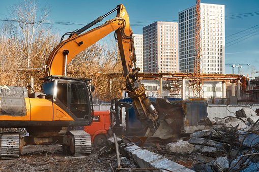 Powerful excavator destroyer removes debris at demolish site under blue sky on winter day