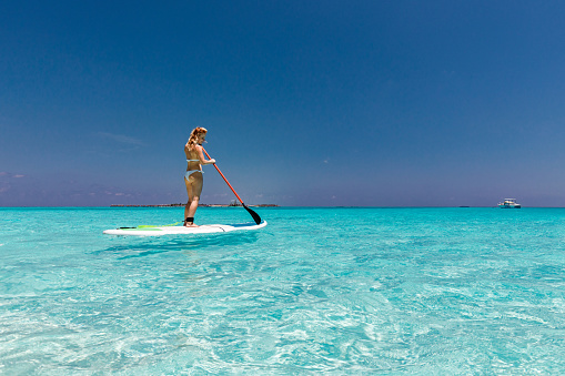 Young woman having fun while stand up paddling in summer day at sea. Copy space.