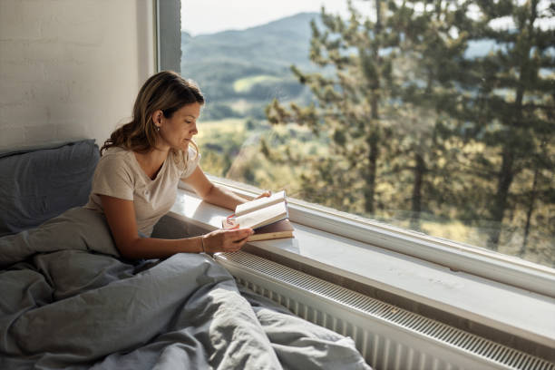 istock Relaxed woman reading a book in bed by the window. 1405953246