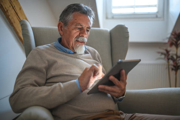 istock Senior Caucasian Man Seated on Comfortable Armchair and Using Tablet 1405953313