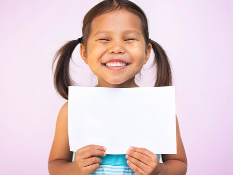 A portrait of a happy asian kid smiling holding a blank paper sign.