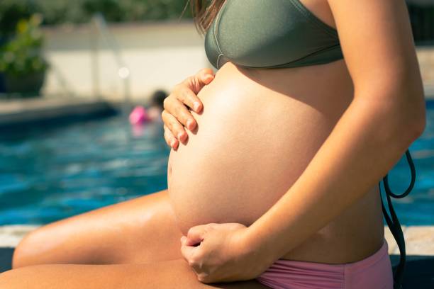 una mujer embarazada disfrutando del sol y el agua, sentada junto a la piscina. relajación prenatal. - swimming pool water people sitting fotografías e imágenes de stock