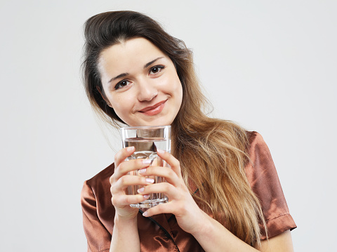 lifestyle, health and people concept - young cute woman wearing pajama holding a glass of water