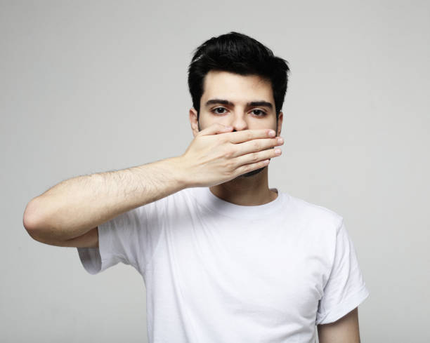 Young handsome man covers mouth with hand Young handsome man covers mouth with hand over grey background sad gay stock pictures, royalty-free photos & images