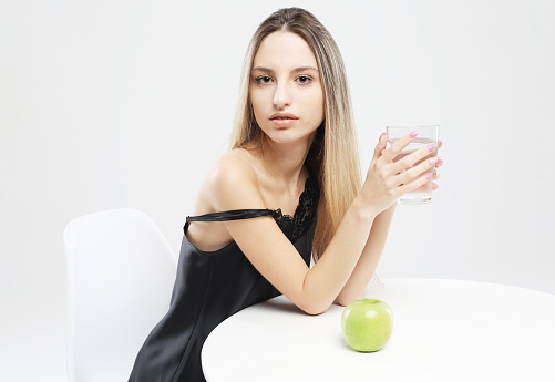 lifestyle, health and people concept - young woman wearing pajamas holding a green apple and a glass of water