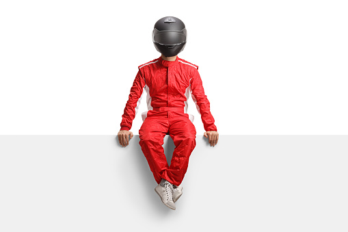 Full length portrait of a male racer with a helmet seated on a blank panel isolated on white background