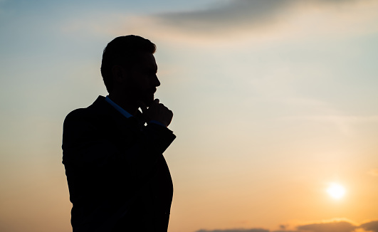 thoughtful man businessman silhouette against sunset sky, copy space, future.