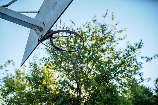 Basketball hoop with a metallic chain net at dawn, defocused trees on the background