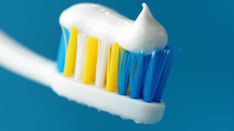 White toothpaste with a beautiful curl at the end squeezed out of a tube on a toothbrush close-up on a blue background. 4k raw macro video.