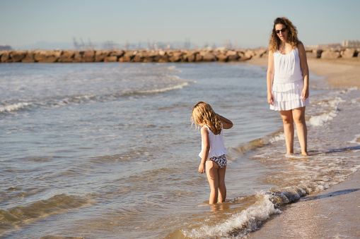 a woman watches her daughter playing with water on the beach