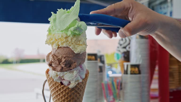 ice cream vendor is filling a ice cream cone with lots of different types of ice cream