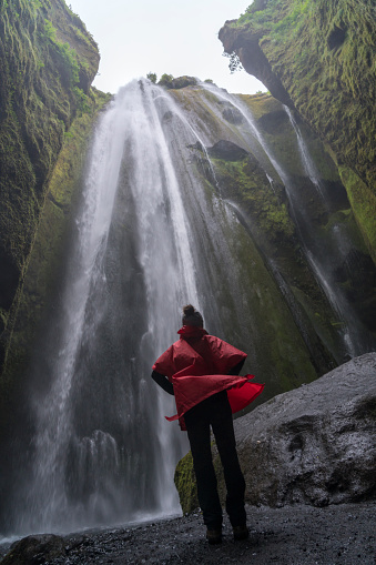 One women in raincoat standing in front of Waterfall Gljúfrabúi,  hidden behind rock fissure, Iceland