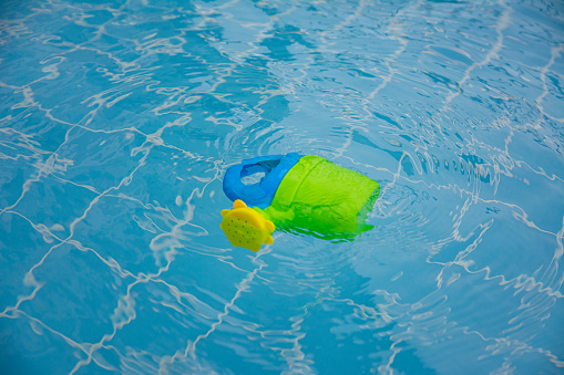A toy watering can floats in the clear water of the pool. A blue tiled bottom and a green-blue baby watering can.