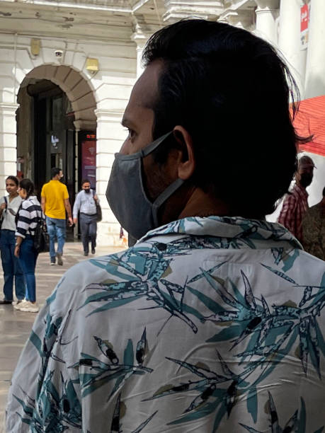 close-up image of indian man, wearing medical face mask, walking across paved retail area, rear view, connaught place, new delhi, india - consumerism indian ethnicity india delhi imagens e fotografias de stock