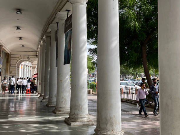 Connaught Place, New Delhi, India - June 23, 2022: Stock photo showing Indian shoppers wearing face mask walking across plaza, through groups of people shopping at Connaught Place, New Delhi, India.