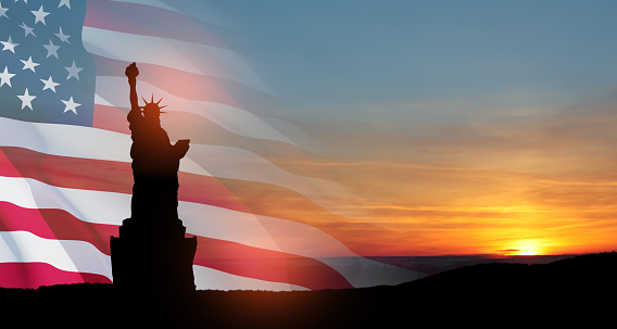 Statue of Liberty with a large american flag and sunset sky on background. Greeting card for Independence Day. USA celebration.