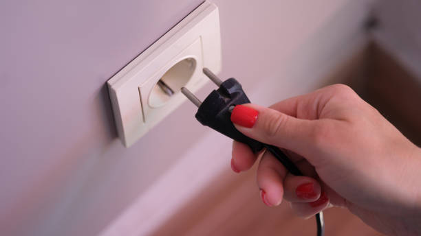 conexión de enchufe eléctrico negro con la mano a un enchufe de plástico blanco en una pared blanca - electric plug outlet pulling electricity fotografías e imágenes de stock