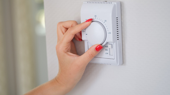 Woman's hand regulating the temperature of central heating of house on thermostat. Indoor climate control
