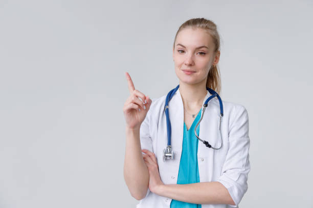 Young european woman wearing doctor with stethoscope pointing with finger up, gesture paying attention stock photo