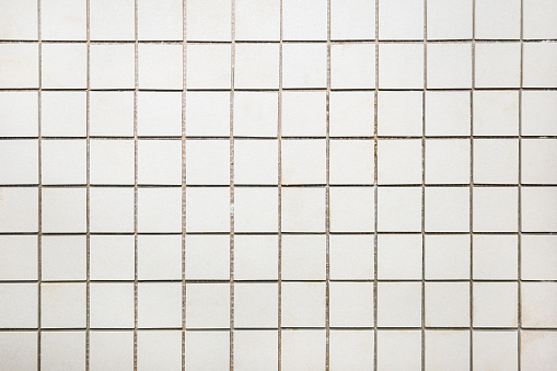 A small square ceramic tile of beige color.Close-up. Square seamless checkered background. Ceramic tiles for cladding.