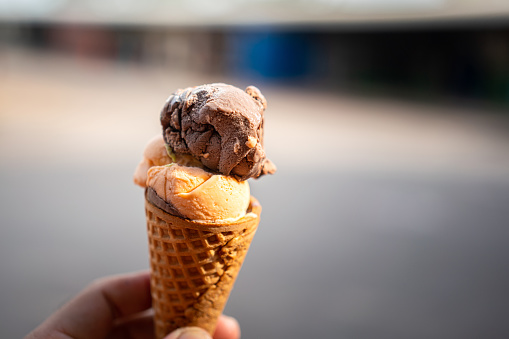 Chocolate ice cream scoop in waffle cone, holding by human hand with blurred background. Food object photo.