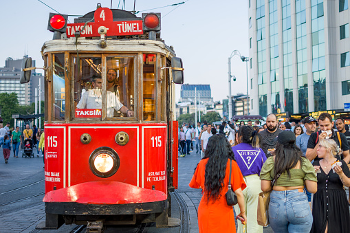 Istanbul, Turkey - June 24, 2022: People walking on Istiklal Avenue in Istanbul, Turkey. The trams, whose name has become identical with Beyoğlu, made their first voyage on February 11, 1914. The tram, which became one of the indispensables of Istiklal Street, succumbed to developing technologies and urbanization and said goodbye to its passengers by making its last voyage on the European Side in 1961 and on the Anatolian Side in 1966. The tram, which was then symbolically re-run on Istiklal Street, continues its journey between Tünel and Taksim, which is its current line. \nPeople travel with this nostalgic tram, take lots of photos and share them on social media.
