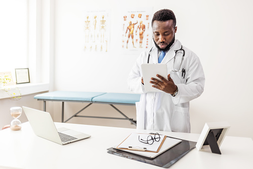 Pensive young male doctor holding digital computer tablet.