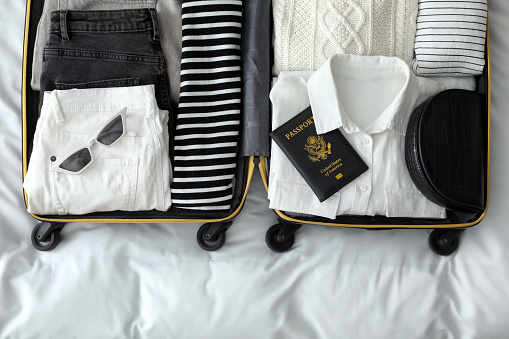 Open suitcase with clothes, passport and accessories on bed, top view