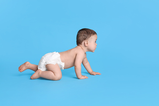 Cute baby in dry soft diaper crawling on light blue background